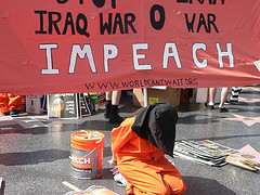 Protester in orange jumpsuit and black hood, kneeling