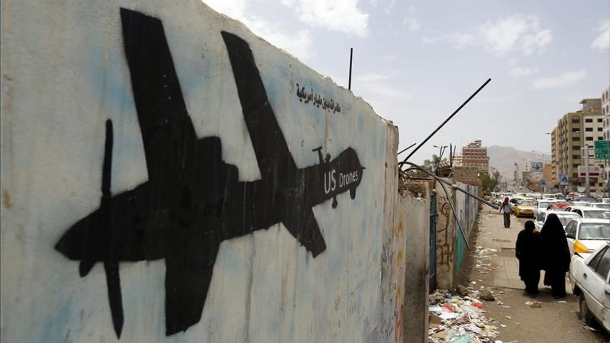 Varios yemens caminan al lado de una pared en la que aparece el grafiti de un dron estadounidense.