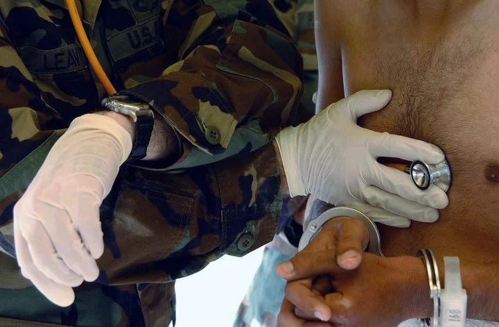 El teniente primero del ejército, Edwin Leavitt, verifica los latidos del corazón de un detenido recién llegado al Campamento X-Ray. Foto Suboficial de primera clase Shane T. McCoy/Marina de los EE. UU. vía The New York Times.