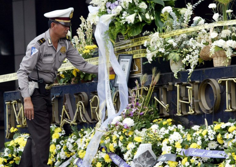 Un oficial de policía indonesio mira los ramos de flores blancas que quedaron en el letrero destrozado del hotel JW Marriott de Yakarta mientras se oraba por los muertos en el atentado de agosto de 2003.